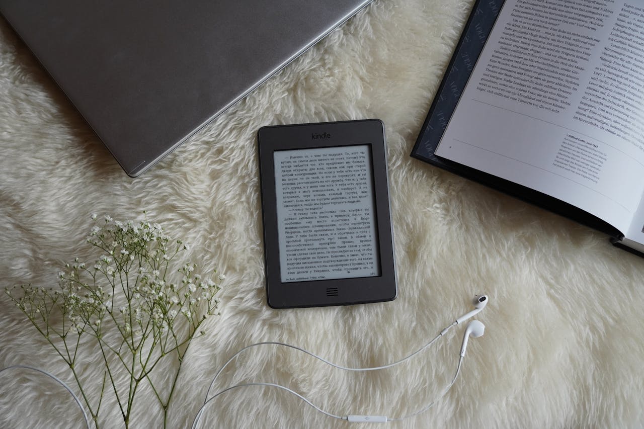 Flat lay of an ebook reader, flowers, and earphones on a fluffy surface for a cozy reading atmosphere.